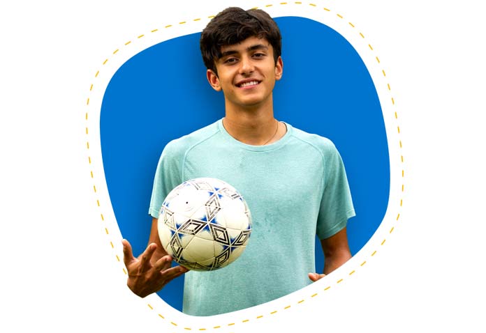 Boy smiling while wearing a teal T-shirt and holding a soccer ball
