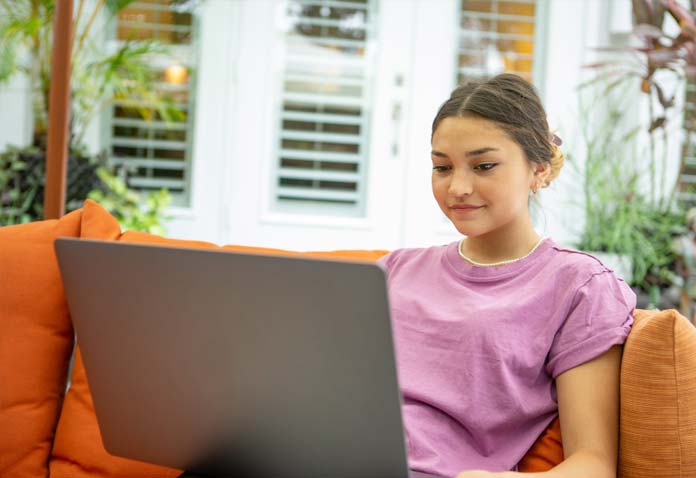 Girl sitting on an orange couch wearing a purple T-shirt and using a laptop
