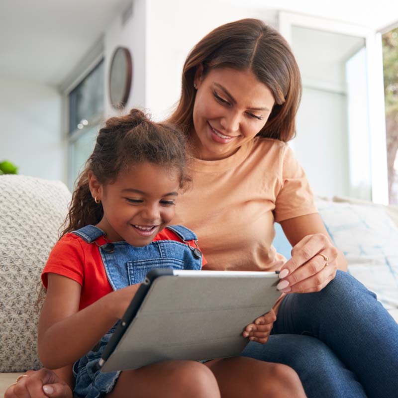 Woman and child sitting on a couch smiling while using a tablet